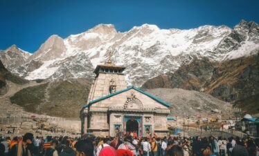 A crowd of pilgrims at Kedarnath Temple with snowcapped Himalayan peaks in the background.